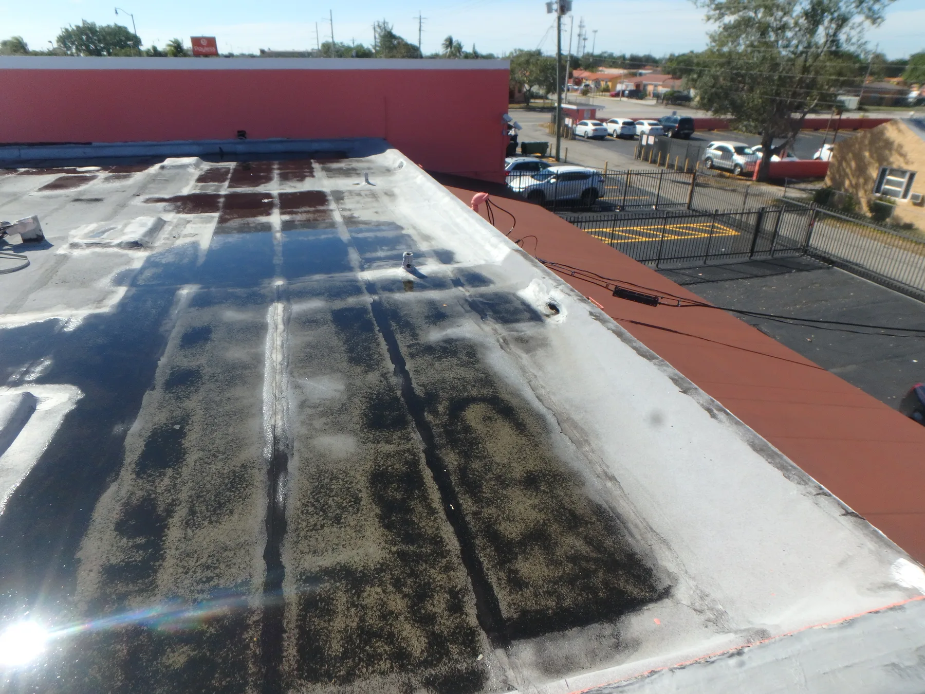 Flat roof of a commercial plaza with patched seams and an adjoining parking lot.